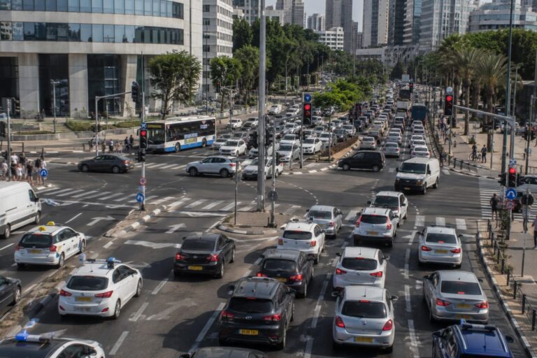 צומת עירוני מרכזי בגוש דן בשעת עומס, עם ריבוי כלי רכב, רמזורים ומעברי חצייה,