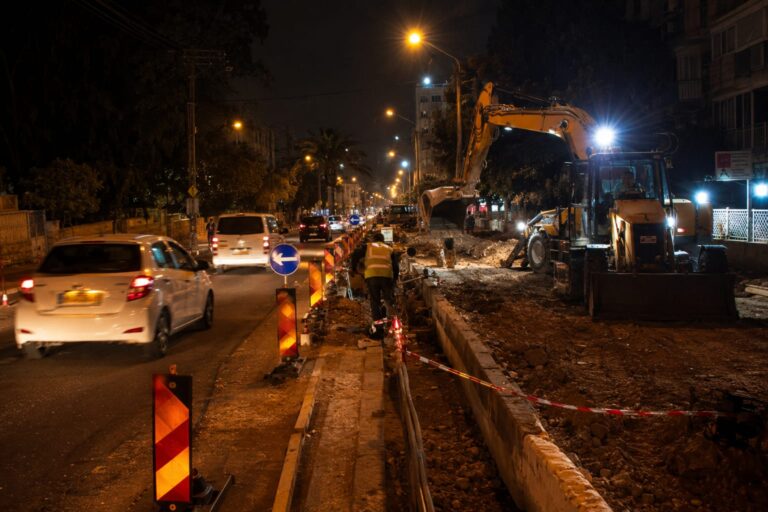 רחוב הרצל ברחובות בשעות הלילה, עם עבודות תשתית, מחסומי תנועה, כלי עבודה ותאורת אתר, בעוד כלי רכב מופנים לדרכים חלופיות
