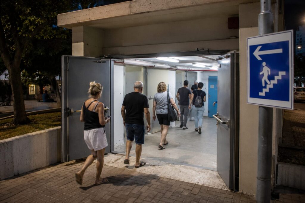 מקלט ציבורי פתוח ברמת גן עם דלתות פתוחות ושילוט הכוונה, לצד תושבים נכנסים למרחב המוגן