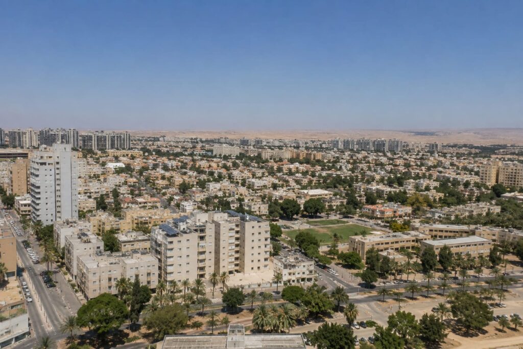נוף עירוני דרומי עם בנייה אופיינית, צמחייה מדברית ורקע של מרחבי הנגב
